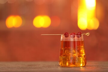 Glass of alcoholic cocktail with garnish on table against blurred background, space for text. Bokeh effect