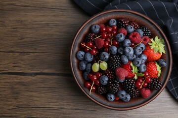 Different ripe berries in bowl on wooden table, top view. Space for text