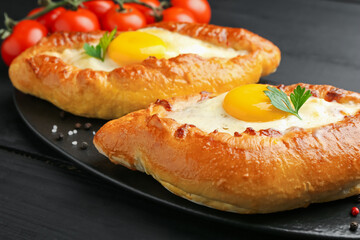 Tasty khachapuri with cheese and eggs on black table, closeup
