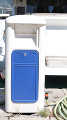 Modern yacht charging station with blue panel and connected hose on a sunny marina dock, vertical