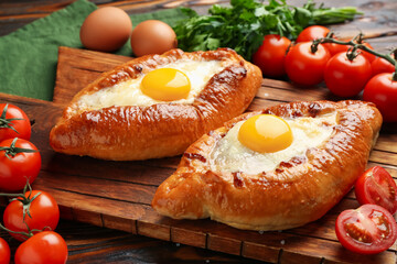 Tasty khachapuri with cheese, eggs and other products on wooden table, closeup