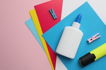 Glue in bottle, color paper and highlighter on pink background, flat lay. Space for text