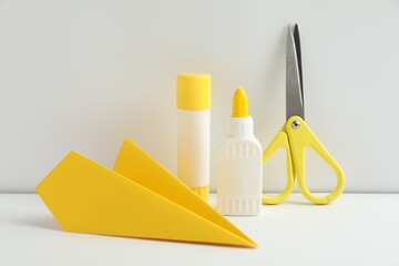 Liquid and stick glue, paper plane, scissors on white table