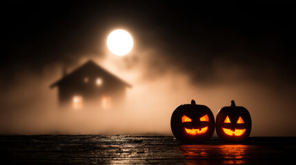 Two glowing jack o lanterns sit on wooden surface with foggy, moonlit house in background, creating spooky Halloween atmosphere
