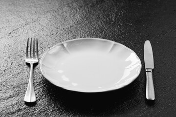 Empty plate with fork and knife on black surface, ready for dining and showcasing minimalistic table setting ideas
