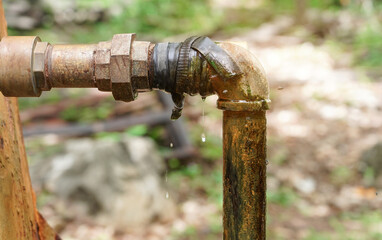 Water leaks from a long-used old rusted metal pipe.