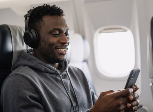 young man enjoying music on headphones while using smartphone during airplane flight