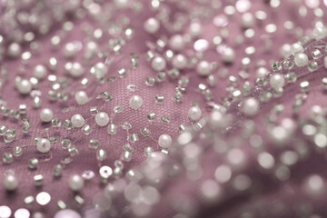 Detailed close-up of pearl pink lace with sequins and beads on delicate mesh, creating a shimmering texture perfect for fashion, couture, and luxury fabric backgrounds