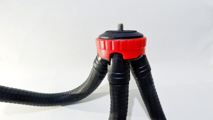 Close-up of a flexible mini tripod with a red and black mount on a white background. Represents photography equipment, camera accessories, and video recording tools concept.