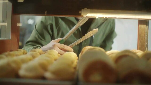 Pinzas tomando pan reci&eacute;n horneado de una vitrina c&aacute;lida.