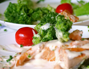 A delicious and healthy meal is served on a white plate, featuring baked salmon and broccoli in a creamy sauce