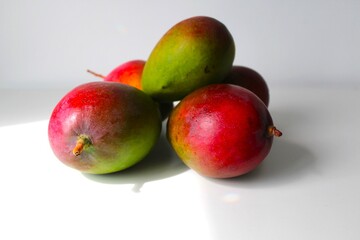 Beautiful and original composition with delicious ripe and tropical mangoes. Healthy and organic food concept. Photo with a white background and hard shadows. With space for text.