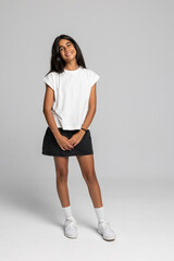 Charming teenage girl posing in casual white t-shirt and black skirt, full body studio shot with smile.