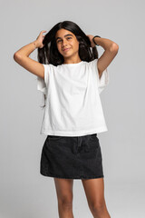 Energetic teenage girl posing playfully with hands in hair, casual white t-shirt and denim skirt studio shot.