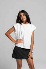 Teenage girl posing confidently in casual white t-shirt and black denim skirt, stylish fashion studio portrait.