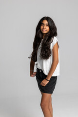 Trendy teenage girl posing with hands in pockets, casual white t-shirt and black denim skirt, cool urban studio portrait.