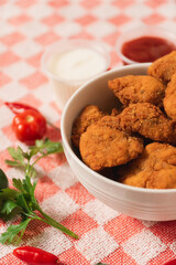 Close-up view of a bowl of nuggets surrounded by vegetables on a checkered tablecloth.