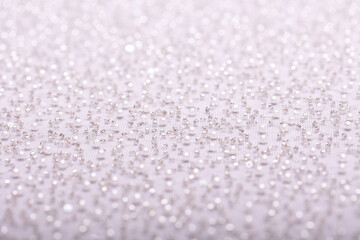 Obraz premium Close-up of elegant, off-white pearl lace fabric with delicate beads and sequins on fine mesh, creating a shimmering texture ideal for fashion, bridal, and luxury design concepts.