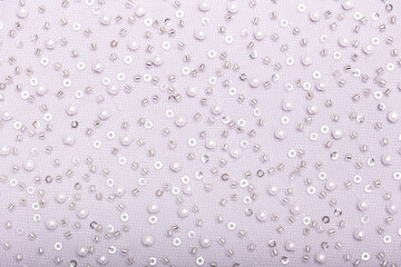 Close-up of elegant, off-white pearl lace fabric with delicate beads and sequins on fine mesh, creating a shimmering texture ideal for fashion, bridal, and luxury design concepts.