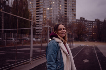 A young woman stands thoughtfully on a deserted urban track during twilight, surrounded by tall apartment buildings