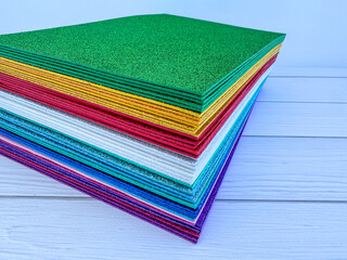 Stack of glitter foam sheets in various colors on white wooden background