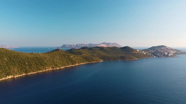aerial footage showcasing the pristine turquoise waters of the Mediterranean Sea meeting the lush, green hills near the charming coastal town of Kaş, Turkey. This breathtaking landscape features a cle