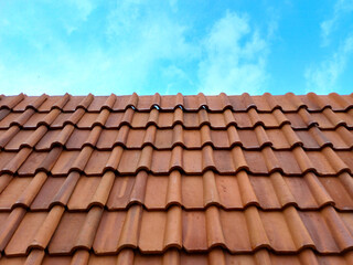 Vibrant, smooth terracotta clay roof tiles set against a clear blue sky on a sunny day. Clean, detailed pattern of red roofing material. Ideal for architecture and construction themes.