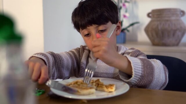 Boy focused on cutting waffle pieces before eating breakfast at home kitchen table