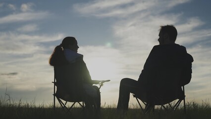 Silhouette of a man and a woman seeing off the sunset together in the sky, hand in hand, family...