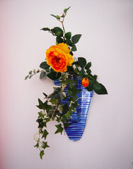 Flower arrangement of yellow roses and ivy in a blue glass pot.