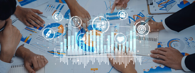 A group of business professionals collaborate over charts and graphs, exemplifying teamwork in data analysis and strategic financial planning in a modern office setting. Trope