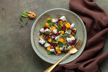 Healthy homemade salad with baked pumpkin, beetroot, spinach, arugula rocket, feta cheese and walnut in a bowl on the table. Top view