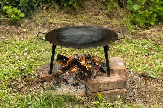 A large, round, flat-bottomed cooking pan called a "discada" or "cowboy wok", typically used in outdoor cooking. It's placed over an open flame made from burning wood or charcoal, supported by bricks.