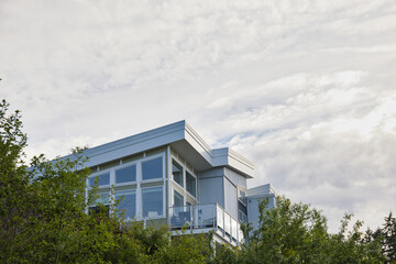 Modern white, grey and green apartment building with glass balconies, nestled among green trees on a clouddy day