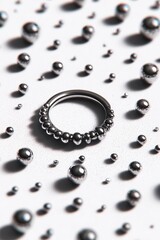 Glossy metal ring with rounded bead texture lies among scattered chrome spheres on a white textured surface