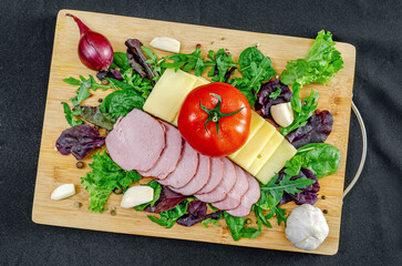 Set board with sliced cheese, ham, tomatoes and peppers, garlic and herbs. Healthy protein menu.