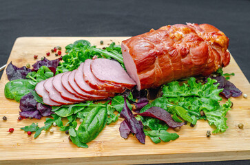 Sliced pieces of baked pork with salad mix, seasonings on wooden board. Delicious meat. Protein.