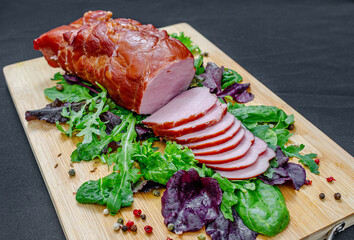 Sliced pieces of baked pork with salad mix, seasonings on wooden board. Delicious meat. Protein.