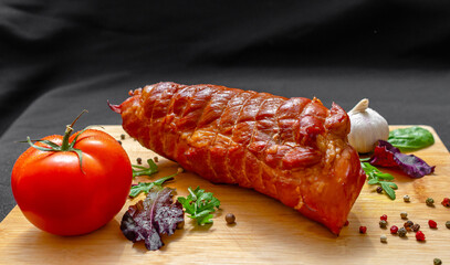 Whole piece of shiny baked pork with salad mix, pepper, tomato and garlic on wooden board, on black.