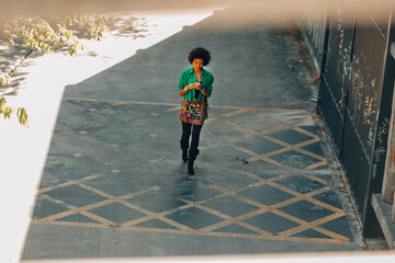 woman with afro hair and mobile phone walking down the street