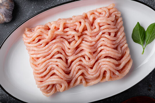 Raw chicken minced meat on cutting board and ingredients. Ground meat with ingredients for cooking on dark background close up. Top view