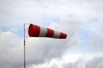 Red and white striped windsock cone shows wind direction and wind speed about 15 knots on aerodrome airfield view close-up