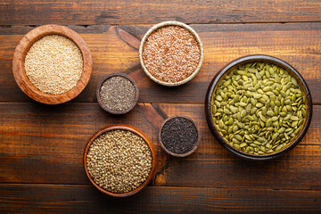 Pumpkin, sesame, flax, hemp, chia seeds in bowls, seeds for good health of mind and body, enriched with minerals and vitamins. Top view, wooden background