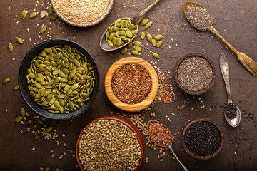 Pumpkin, sesame, flax, hemp, chia seeds in spoons and bowls, seeds for good health of mind and body, enriched with minerals and vitamins. Top view, dark background