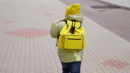 little schoolgirl runs along the path with backpack on her shoulders. back view. slow motion. girl returns school for lesson. autumn, spring season. kid likes to run actively recess. Kid job concept.