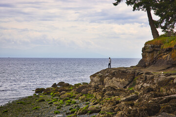 Men stands on a rocky shoreline dangerously close to the water.