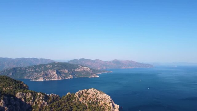 aerial view captures the serene blue waters of the Aegean Sea meeting the rugged, forested coastline near Turunc, Turkey. This beautiful landscape showcases the natural beauty of the Turkish Riviera, 