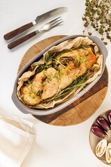 A beautifully plated oven-baked fish dish sits nestled in parchment paper, adorned with herbs and served with roasted eggplants. Ready to eat, the dish is presented on a wooden board