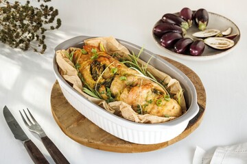 A juicy, baked chicken roll filled with herbs is presented in a ceramic dish. It is accompanied by...