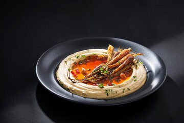 This is a close-up of a plate of creamy hummus surrounded by roasted baby carrots and flavored with chili oil. Fresh herbs and spices are sprinkled on top for an exquisite presentation